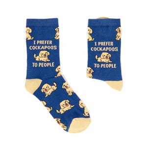 Peut inclure: Une paire de chaussettes bleu marine avec un motif répétitif de chiens Cockapoo beige clair et le texte I PREFER COCKAPOOS TO PEOPLE en jaune. Les chaussettes présentent un talon et une pointe de couleur beige clair contrastant avec le bleu.
