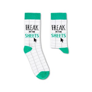 May include: A pair of white socks with a green cuff and a grid pattern. The socks have the text "Freak in the Sheets" with a cursor arrow printed on them.