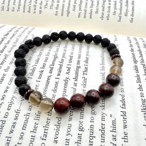May include: A beaded bracelet featuring dark brown lava rock beads, smoky quartz, and deep red-brown gemstone beads. The bracelet is strung on a durable cord, showcasing a natural and earthy aesthetic.