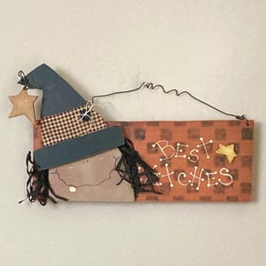 May include: Wooden Halloween sign featuring a witch with a blue hat, a star, and the words "Best Witches" in white. The sign has a rustic, handmade appearance, perfect for seasonal decor.