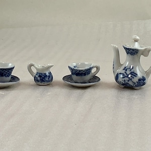 May include: A miniature porcelain tea set with blue floral patterns. The set comprises a teapot, two teacups with saucers, and a creamer. The teapot features a lid and a curved handle. The teacups and creamer share a blue floral design.