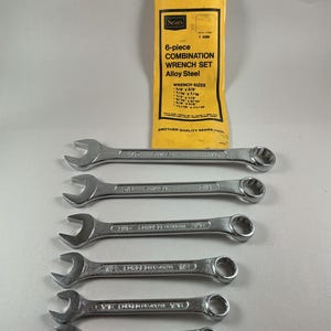 Könnte beinhalten: Ein sechsteiliges Sears-Kombinationsschlüsselsatz aus legiertem Stahl. Die silbernen Schraubenschlüssel sind in einer Reihe angeordnet. Das Set enthält die Schlüsselgrößen 3/8 x 3/8, 7/16 x 7/16, 1/2 x 1/2, 9/16 x 9/16 und 11/16 x 11/16. Das Set wird in einem gelben Beutel geliefert.