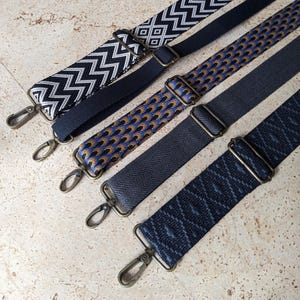 Könnte beinhalten: Vier gemusterte Taschenriemen in verschiedenen Designs. Die Riemen weisen eine Mischung aus Farben wie Marineblau, Schwarz und Beige auf. Jeder Riemen hat Metallbeschläge, einschließlich verstellbarer Schnallen und Verschlüssen.