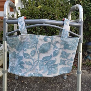May include: A walker with a teal and white floral patterned fabric bag attached to the frame.