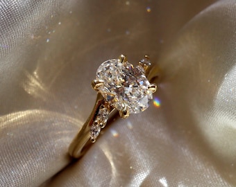 May include: A gold engagement ring with a large oval-shaped diamond and smaller diamonds set in a band.
