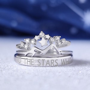 May include: A silver ring set with a star design and the inscription "To the stars who..." The ring is on a white surface with a blue background.
