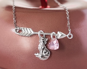 Op de afbeelding: Een zilveren ketting met een vos-bedel, een roze hart-bedel en een pijl-bedel. De ketting ligt op een roze achtergrond.