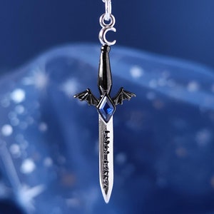 May include: A silver necklace with a black sword pendant featuring a blue gemstone and bat wings. The sword has an inscription that reads "Faster, Faster, Faster".