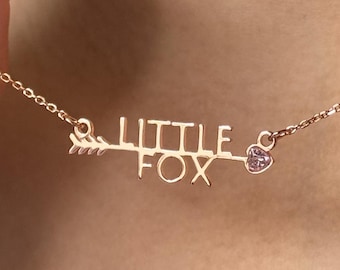Op de afbeelding: Een ketting van roségoud met een delicate ketting en een hanger met de tekst "LITTLE FOX" met een pijl en een klein hartje met een roze steentje.