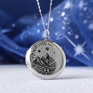 May include: A silver locket necklace with a detailed design of mountains, stars, and a crescent moon. The locket is round and has a hinged opening.