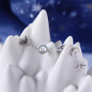 May include: A silver chain bracelet with a moon and star charm, a round iridescent gemstone, and a crescent moon charm.