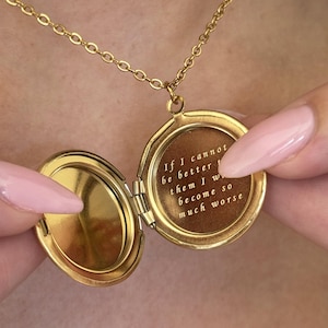 May include: A gold-colored locket necklace with an open, round pendant. The pendant reveals engraved text: "If I cannot be better than them I will become so much worse."