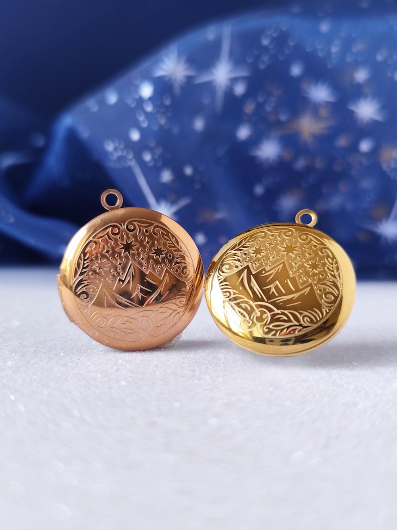 May include: Two round lockets with a star and mountain design. One locket is gold and the other is rose gold.