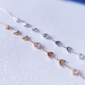 May include: Two delicate gold and silver necklaces with moon and star charms. The necklaces feature a moonstone pendant and are layered on a white background.