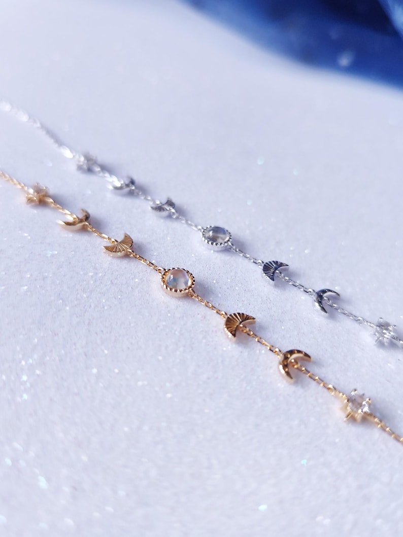 May include: Two delicate gold and silver necklaces with moon and star charms. The necklaces feature a moonstone pendant and are layered on a white background.