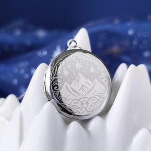 May include: A silver locket necklace with an engraved design of a mountain range and stars. The locket is round and has a hinged lid.