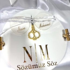 May include: White round serving tray with gold accents and handles. The tray features gold lettering that reads "N|M Sözümüz Söz". Two small white circles with names and a gold scissor charm are attached with ribbons. A pearl beaded strand is also attached.