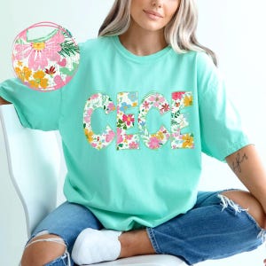 May include: A turquoise t-shirt with the name "Cece" spelled out in large, colorful floral letters.