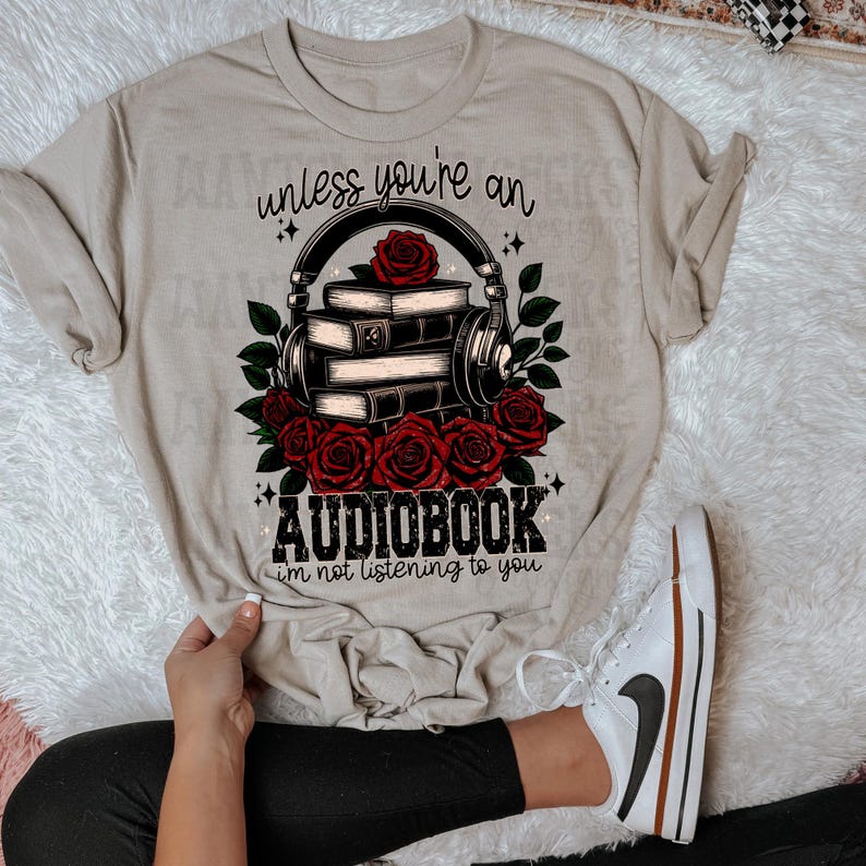 May include: Beige t-shirt with a graphic of a stack of books with headphones and roses. The text reads "unless you're an audiobook, i'm not listening to you."