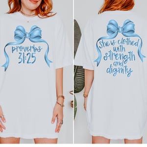 May include: White t-shirt with a blue bow and the text "Proverbs 31:25" on the front. The back of the shirt has a blue bow and the text "She is clothed with strength and dignity".