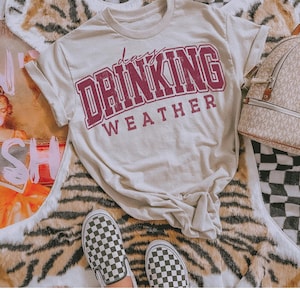 May include: A light beige t-shirt with a maroon graphic that says "lazy drinking weather".