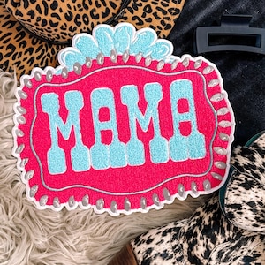 May include: Pink and blue embroidered patch with the word "MAMA" in a vintage style font. The patch is surrounded by a white border with silver studs.