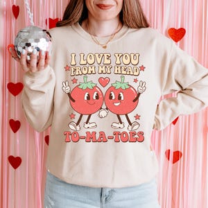 May include: Beige sweatshirt with the text "I Love You From My Head To-Ma-Toes" and a graphic of two cartoon tomatoes holding hands. The tomatoes are red with green tops and smiling faces. The sweatshirt has a crew neck.
