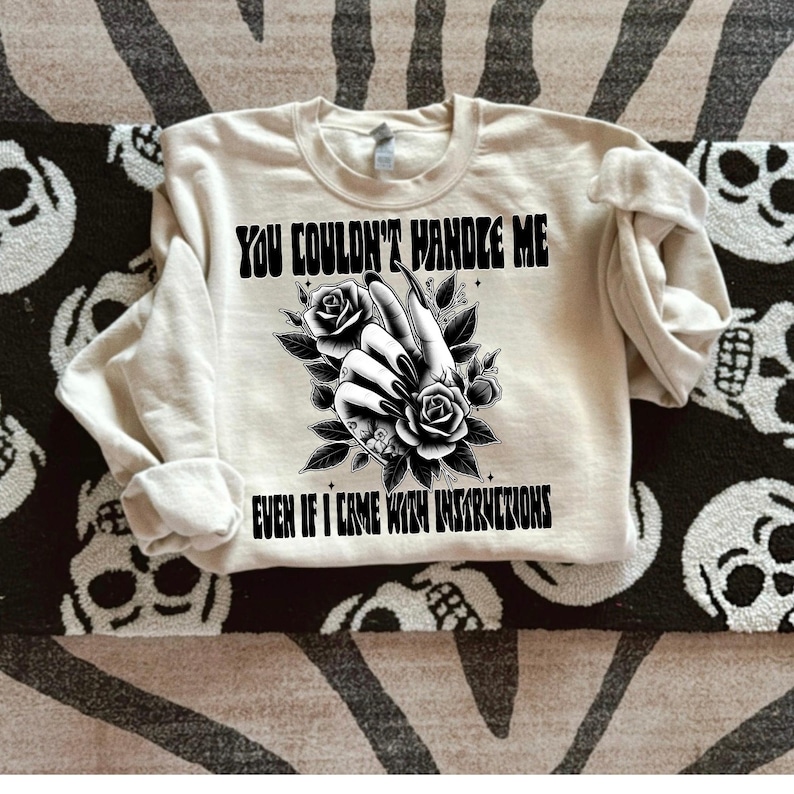 May include: A cream colored sweatshirt with black text that reads "You couldn't handle me even if I came with instructions". The text is surrounded by a black and white illustration of a hand with long nails and flowers.