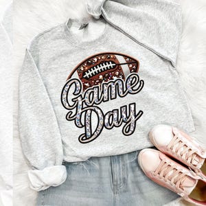 May include: A gray sweatshirt with a brown football design and the text "Game Day" in silver glitter.