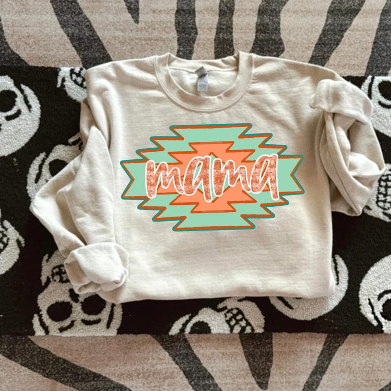 May include: A beige sweatshirt with a graphic design of a turquoise and orange geometric pattern with the word "mama" in the center.