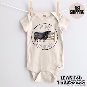 Pode incluir: Um macacão de bebê de cor creme com uma ilustração em preto e branco de uma vaca em frente a um portão. O texto "Future Gate Opener" é impresso em um círculo preto ao redor da vaca.