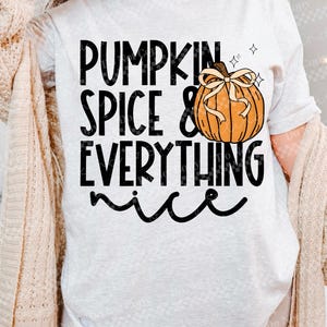 May include: A light gray t-shirt with the text "PUMPKIN SPICE & EVERYTHING nice" in black. A cartoon pumpkin with a bow is to the right of the text. The pumpkin is orange with a brown stem and a tan bow.