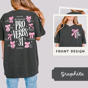 May include: Black t-shirt with a pink and white graphic design featuring the text "PRO VERBS 31" and a series of pink bows with text on each bow. The text on the bows includes phrases like "Stay humble", "Seek wisdom", "Keep serving", "Be virtuous", "Stay strong", "Stay diligent", "Be honest", "Be faithful", "Be disciplined", and "Seek the Lord".