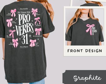 May include: Black t-shirt with a pink and white graphic design featuring the text "PRO VERBS 31" and a series of pink bows with text on each bow. The text on the bows includes phrases like "Stay humble", "Seek wisdom", "Keep serving", "Be virtuous", "Stay strong", "Stay diligent", "Be honest", "Be faithful", "Be disciplined", and "Seek the Lord".