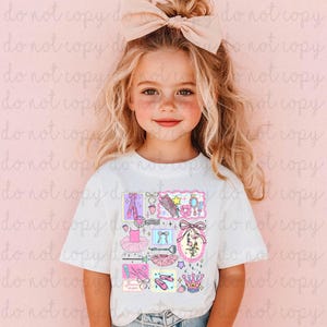 Könnte beinhalten: Ein weißes T-Shirt mit einer Collage von Ballettthemen in Rosa, Lila und Gelb. Das Design umfasst Ballettschuhe, Tutus, Schleifen und Kronen. Das Shirt wird von einem jungen Mädchen mit blonden Haaren und einer großen rosa Schleife getragen.