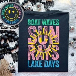 May include: Black t-shirt with a pink and yellow graphic design that says "Boat Waves Sun Rays Lake Days".