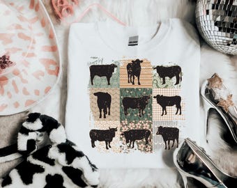 Peut inclure: T-shirt blanc avec un motif patchwork représentant des silhouettes noires de vaches. Le patchwork est composé de différents motifs floraux et géométriques dans des tons de vert, marron et rose.