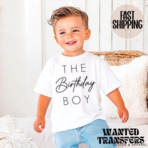 May include: White short-sleeved t-shirt with black text that reads "The Birthday Boy". A young child is wearing the shirt.