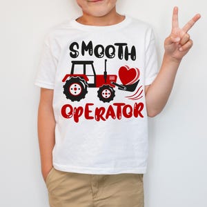May include: White t-shirt with a red tractor design and the text "SMOOTH OPERATOR" in black. The tractor is scooping up a red heart.