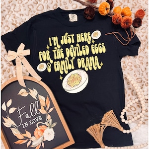 May include: Black t-shirt with a yellow graphic that says "I'm just here for the deviled eggs & family drama". The graphic also includes a cartoon deviled egg.