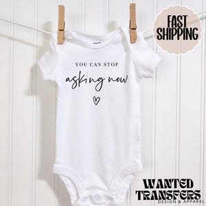 May include: White baby onesie with black text that reads "You can stop asking now" with a small heart below the text.