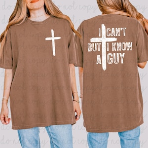 May include: Brown short-sleeved t-shirt with a white cross on the front and the text "I CAN'T BUT I KNOW A GUY" on the back. The shirt is a relaxed fit and made of a soft material.