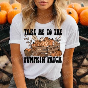 May include: White t-shirt with the text "TAKE ME TO THE PUMPKIN PATCH" in black and brown. The graphic features a wooden crate filled with pumpkins, a caramel apple, and fall foliage.
