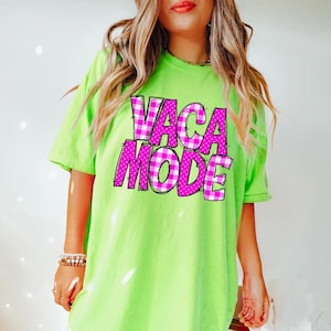 May include: A neon green t-shirt with the words "VACA MODE" in a pink plaid and polka dot design. The shirt has short sleeves and a relaxed fit, perfect for a casual summer look.