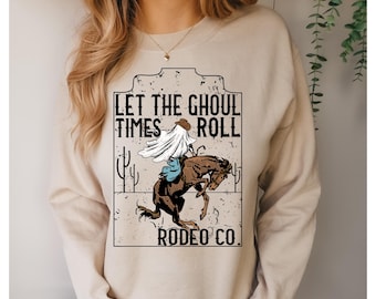 May include: Beige sweatshirt with a graphic featuring a ghost riding a bucking bronco. The text reads "LET THE GHOUL TIMES ROLL RODEO CO." The design includes cacti and a cowboy hat. A fun, spooky design for Halloween.