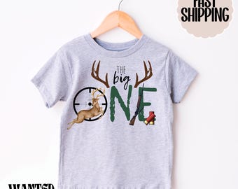 May include: A grey t-shirt with a green number one, a deer, a rifle, and the text "The Big One".