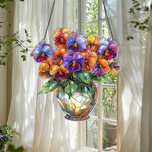 May include: A stained glass window hanging with a colorful bouquet of pansies in a vase. The pansies are purple, yellow, orange, and red. The vase is a mosaic of different colored glass.