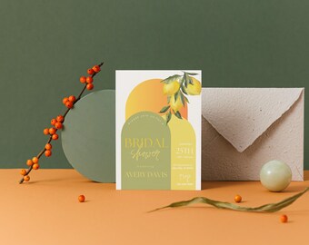 May include: A white card with a lemon illustration and the text "Bridal Shower" in gold lettering. The card is on a light orange surface with a green background.