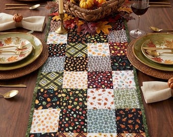 May include: A rectangular table runner featuring a patchwork design of various autumn-themed fabric squares in shades of orange, yellow, brown, black, and green. The runner has a dark green border and is displayed on a wooden dining table.