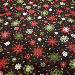 May include: A black fabric featuring a repeating pattern of snowflakes in shades of red, lime green, and white. The design includes intricate, varied snowflake shapes interspersed with small dots and thin, curved lines across the surface.